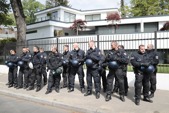 Mehrere Polizisten stehen in einer Reihe vor dem Zaun einer großen Villa