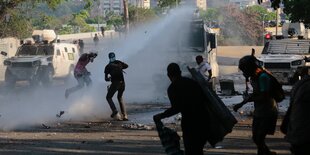 Regierungskritische Demonstranten werfen Steine auf einen Wasserwerfer.