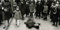Schwarz-weiß-Foto: Ein Mann liegt auf der Straße, Kinder stehen um ihn herum