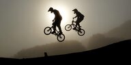 Zwei BMX-Fahrer machen einen Trick auf einer Schanze vor einem Sonnenuntergang