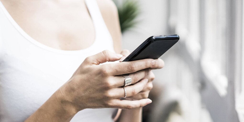 Eine Frau hält ein Smartphone in der Hand und steht vor einem Fenster