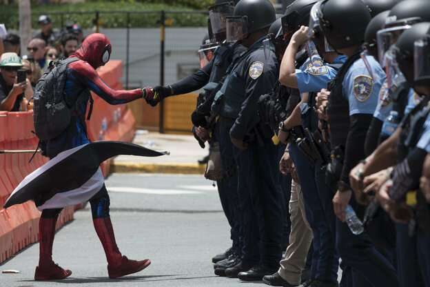 Ein Demonstrierender, verkleidet als Spiderman, geht auf eine Blockade von Polizeibeamten zu und reicht einem Polizisten die Hand.