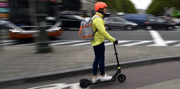 Eine Frau mit Helm fährt mit einem elektronischen Roller auf einem Fahrradweg