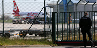 Polizist auf einem Flughafen. Hinter dem Zaun wird ein Flugzeug abgefertigt.