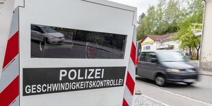 Ein Auto fährt an einer mobilen Geschwindigkeitsmessanlage mit der Aufschrift "Polizei - Geschwindigkeitskontrolle" vorbei.