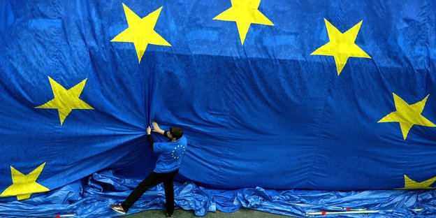 Ein Mann zerrt an einer riesengroßen Europafahne