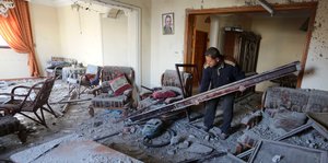 Ein Mann versucht in einer zerstörten Wohnung aufzuräumen