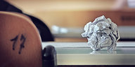 Zerknülltes Rechenpapier auf einem Tisch, Ausschnitt einer Rückenlehne eines Schreibtischstuhls