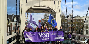 Eine Gruppe von Menschen halten ein lila Transparent auf einer Brücke