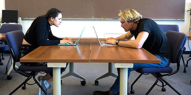 An einem Schreibtisch sitzen zwei Personen vor Laptops