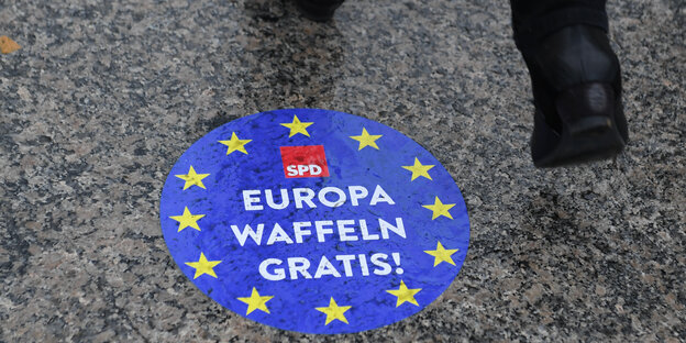 Ein Mensch läuft über einen SPD-Aufkleber mit der Aufschrift „Europa Waffeln gratis!“