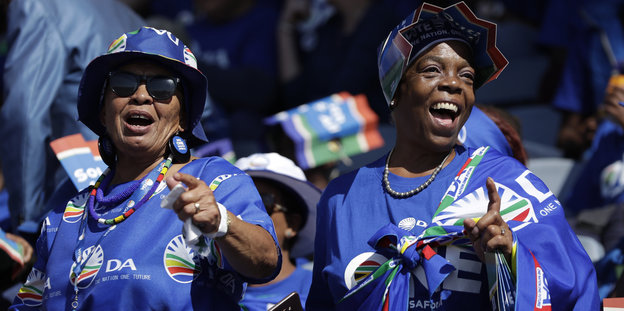 Zwei Frauen in blauer Kleidung tanzen auf einer Wahlkampfveranstaltung