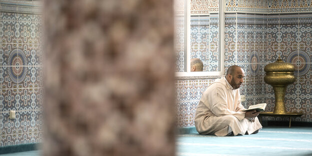 Ein Mann sitzt im Schneidersitz auf dem Boden und hält einen Koran in der Hand
