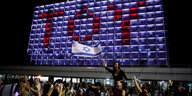 Auf einem Gebäude ist der Schriftzug "TOY" zu lesen, davor sind feiernde Menschen zu sehen, von denen eine Person eine Israelfahne schwingt
