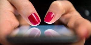 Nahaufnahme eines Smartphone-Displays auf dem jemand mit rot lackierten Fingernägeln tippt.
