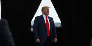 Trump steht vor einem Spalt zwischen zwei dunklen Vorhängen