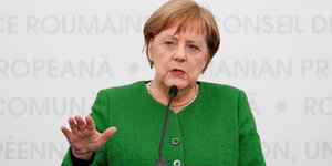 Merkel in grüner Kleidung macht mit der Hand ein abbremsendes Zeichen