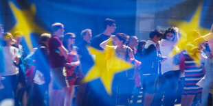 Menschen spiegeln sich in einem Fenster mit einer europäischen Flagge im Europäischen Parlament