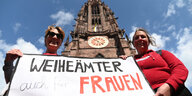 Zwei Frauen stehen vor dem Freiburger Münster und halten ein Banner mit der Aufschrift "Weiheämter auch für Frauen" in die Höhe
