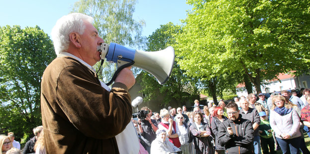 ein Mann spricht vor einer Menschenmenge in ein Megafon