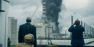 Szene aus "Chernobyl": Drei Personen, von hinten zu sehen, betrachten eine dunkle Rauchwolke