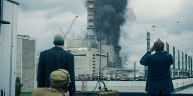 Szene aus "Chernobyl": Drei Personen, von hinten zu sehen, betrachten eine dunkle Rauchwolke