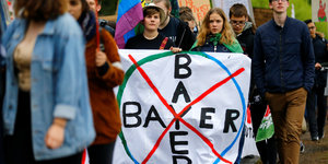 Umweltaktivisten protestieren mit einem weißem Banner, auf dem ein durchgestrichenes Bayer-Logo zu sehen ist.