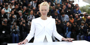 Tilda Swinton trägt einen weißen Anzug. Hinter ihr zahlreiche Fotografen