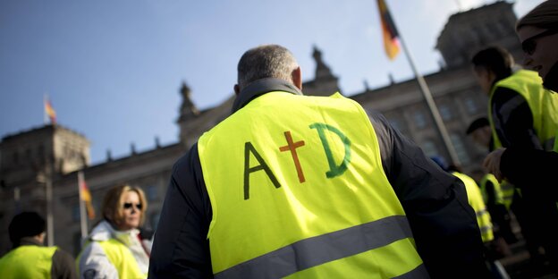 Ein Demonstrant trägt die Buchstaben AfD auf der Gebweste, das f ist als Kreuz dargestellt