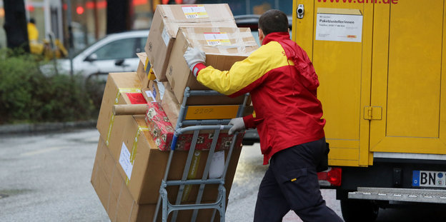 Paketbote schiebt eine Ladung Pakete von einem gelben Lastwagen weg