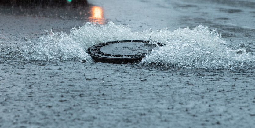 Wasser quillt aus einem Gullideckel