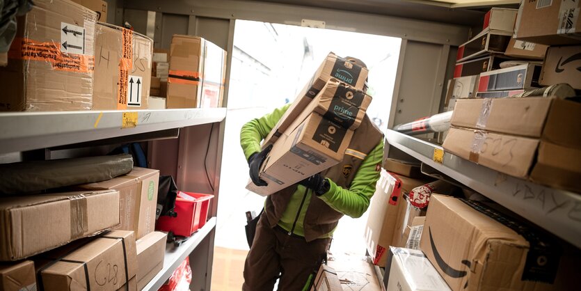 Im der Tür des Laderaums eines Paketautos steht ein Zusteller, den Arm voller Pakete.