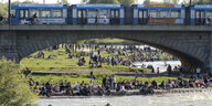 Personen am Ufer der Isar in München. Über die Bögen der Reichenbachbrücke fährt die Trambahn