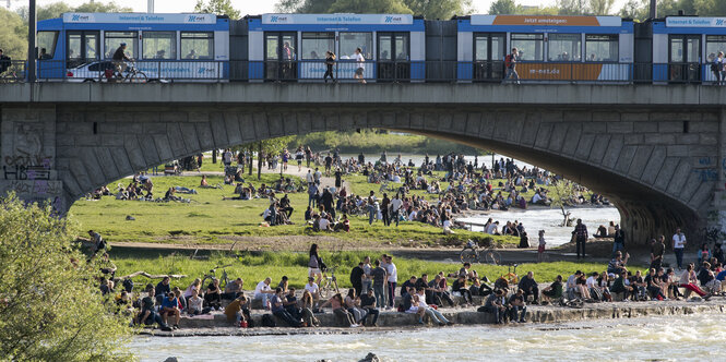 Personen am Ufer der Isar in München. Über die Bögen der Reichenbachbrücke fährt die Trambahn