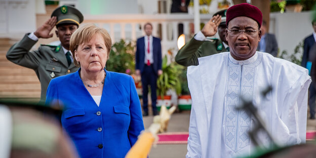 Eine Frau (Angela Merkel) steht neben einem Mann (Mahamadou Issoufou). Im Hintergrund salutiert ein Soldat