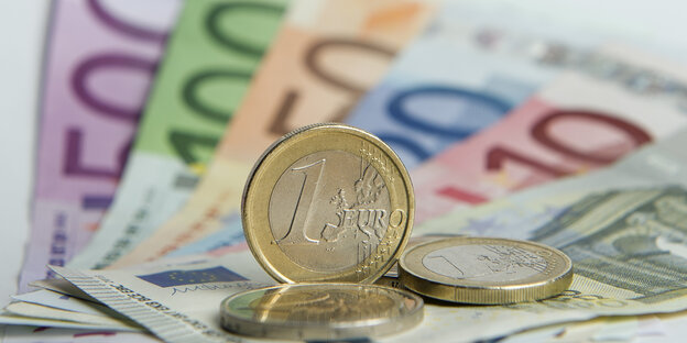 Eine gläneznde Ein-Euro-Münze steht auf Geldscheinen aus Papier