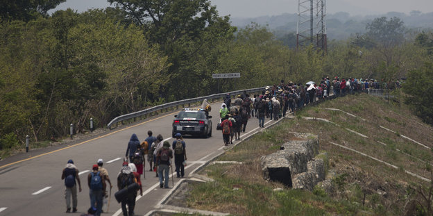 Migranten aus Mittelamerika gehen mit Rucksäcken auf dem Rückeneine Straße entlang
