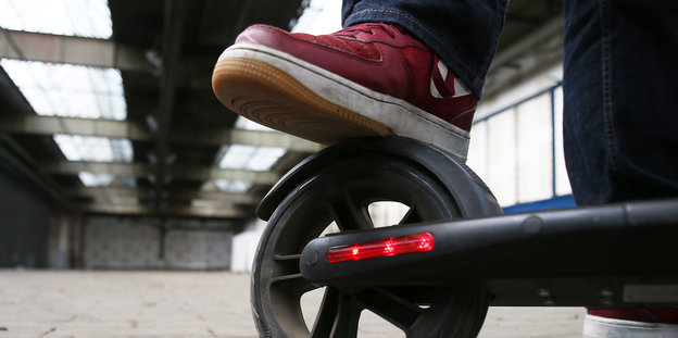 Auf dem Rad eines E-Scooters setzt eine Person ihren Fuß ab