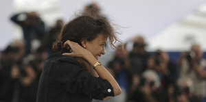 Eine Frau mit zersausten Haaren vor Fotografen
