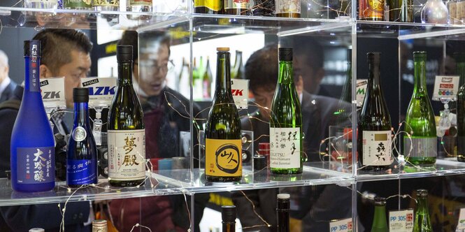 Mehrere Alkoholflaschen in verschiedenen Farben und mit japanischen Etiketten in einem Glasregal