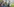 Zwei Männer inspizieren ihre Waffen, im Hintergrund ein Bergpanorama und ein See