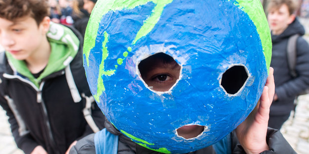 ein Kind hat sich eine Weltkugel aus Pappmaschee über den Kopf gestülpt