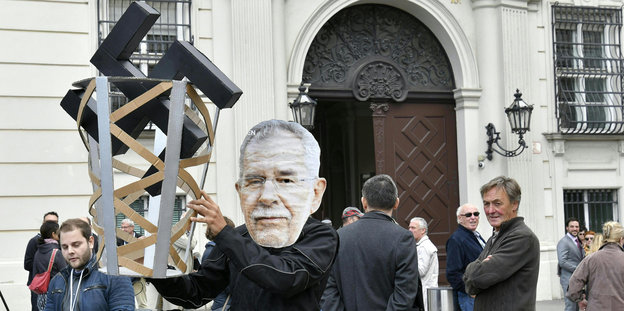 ein Demonstrant mit Van der Bellen-Maske hält einen Papierkorb hoch, in dem ein großes Hakenkreuz steckt