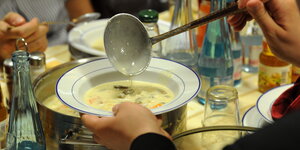 auf einem voll gedeckten Tisch schöpft jemand Suppe in einen Teller