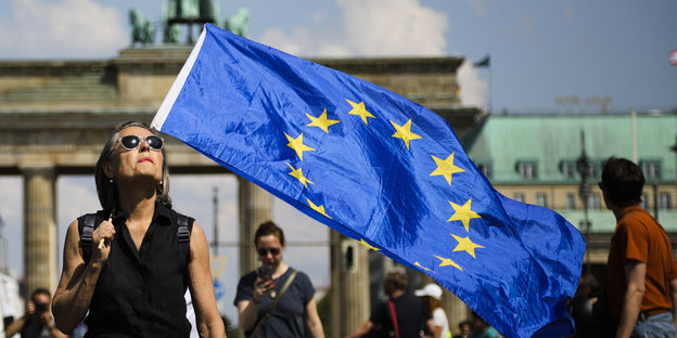 Eine Demonstrantin hält eine Flagge der EU vor dem Brandenburger Tor und blickt in die Sonne