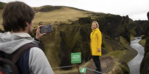 Eine Frau steht in Island hinter einer Absperrung und in dem Canyon lässt sich von einem Mann mit Smartphone fotografieren
