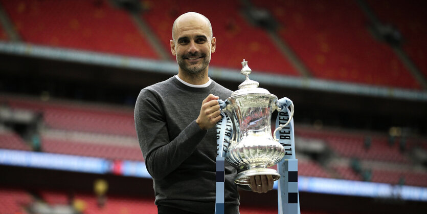 Fußballtrainer Pep Guardiola hält nach dem Sieg seines Vereins im FA-Cup-Finale den Pokal hoch.