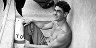 Der Schwimmer Alfred Nakache ist auf einem Schwarz-Weiß-Foto zu sehen, wie er mit nacktem Oberkörper auf einer Treppe sitzt