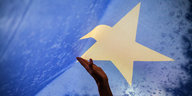 Eine Hand greift nach einem Stern auf einer EU-Flagge