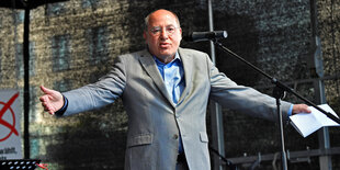 Gregor Gysi breitet auf einer Bühne die Arme aus